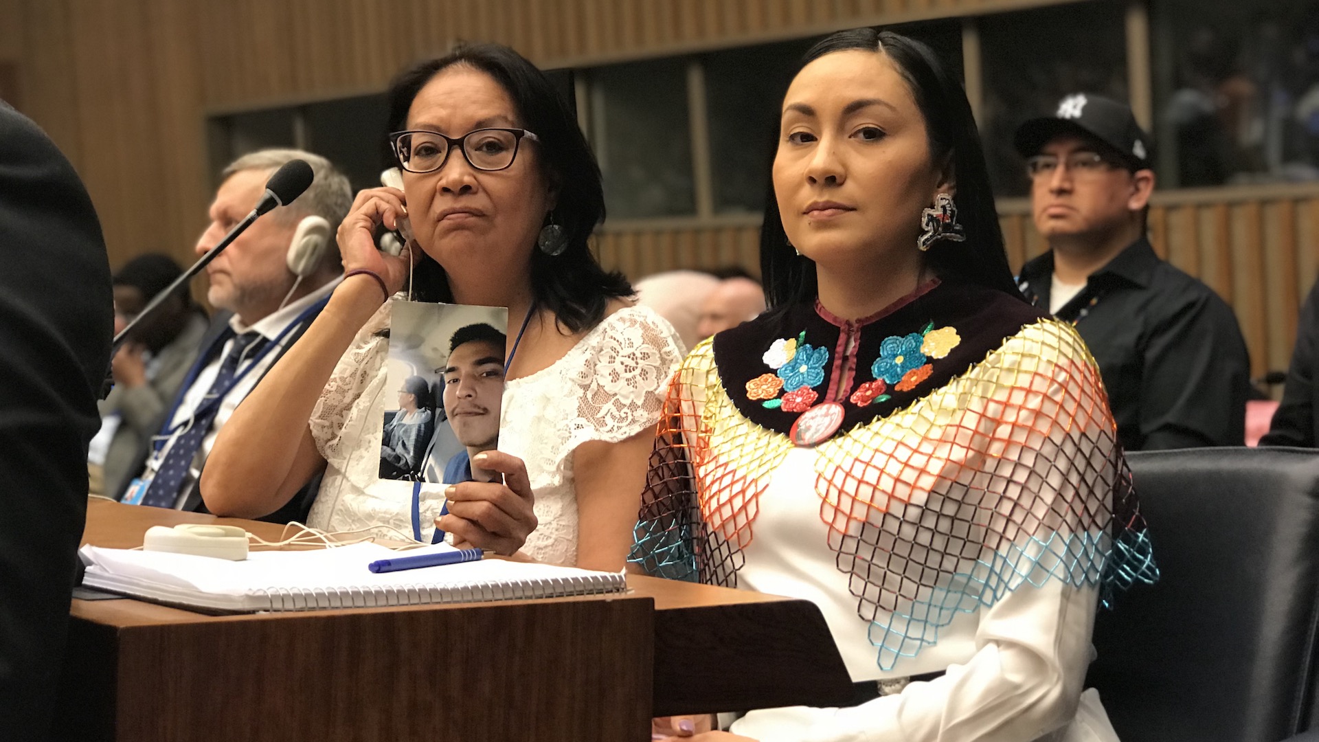 Nîpawistamâsowin We Will Stand Up: People at microphone holding up a portrait