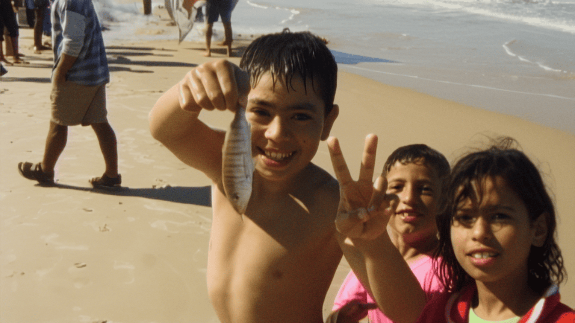 Children smiling on a beach in Gaza in With Hasan in Gaza by Kamal Aljafari