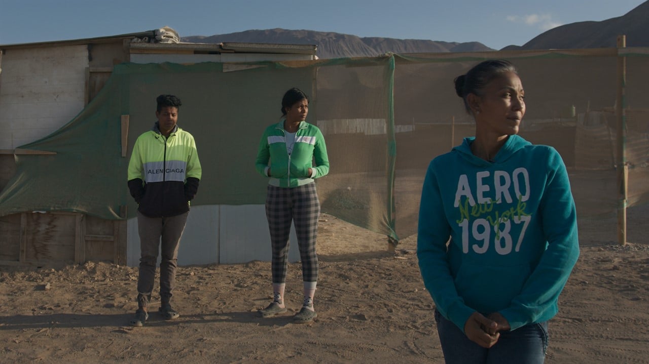 Three people stand in front of a tent in a desert-like camp, still from the Documentary Unwelcomed