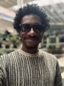 Brahim Snoopy, one of the directors of the documentary Khartoum, smiling and wearing sunglasses indoors.