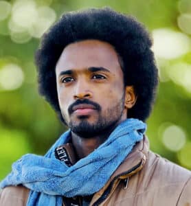 Timeea M. Ahmed, one of the directors of the documentary Khartoum, standing outdoors wearing a brown jacket and blue scarf.